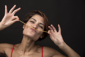 Bellissima e simpatica donna in costume tiene con le due mani degli spaghetti sulla bocca e fa le...
