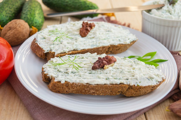 Nutritious sandwich with cottage cheese paste on rye bread on a white plate.