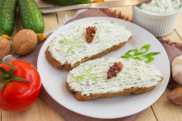 Nutritious sandwich with cottage cheese paste on rye bread on a white plate.