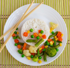 Rice with vegetables steamed on a white plate, laid out in a circle. Vegan. The top view.