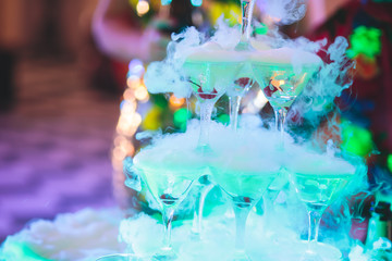 Beautiful pyramid line of multicolored different colored alcohol cocktails with mint on a tropical style party, martini, vodka,and others on decorated catering bouquet table on open air event