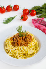 Spaghetti bolognese on white plate on white table.