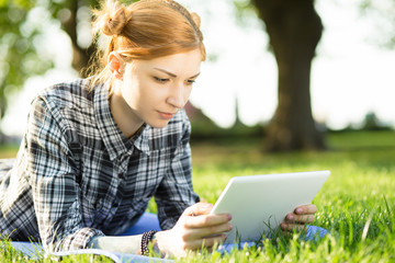 Young woman lying on grass in park and using digital tablet