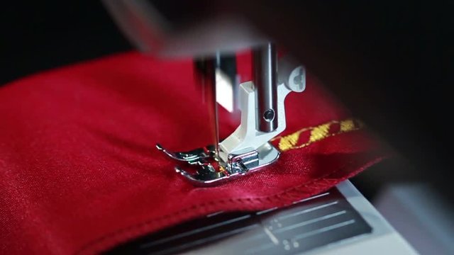 Sewing needle stitching seam on fabric in slow motion. Sewing machine in action. Yellow thread pattern on red fabric. Sewing machine embroider pattern on the fabric. Sewing machine slow motion