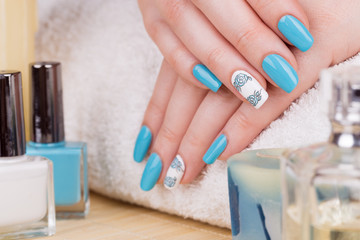 Manicure - Beauty treatment photo of nice manicured woman fingernails with blue polish and flower design on accent nail.