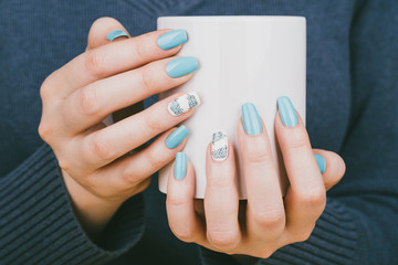 Manicure - Beauty treatment photo of nice manicured woman fingernails holding a cup. Nice blue polish and flower design on accent nail.