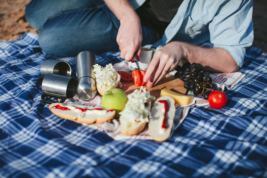 picnic on the plaid. Man prepares sandwiches with tomatoes
