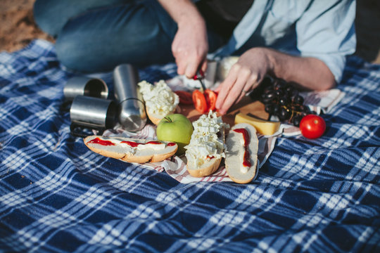 picnic on the plaid. Man prepares sandwiches with tomatoes