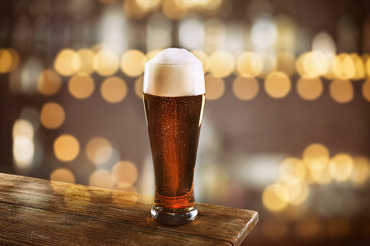 Glass of cold fresh beer on table, on dark pub background