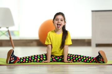 Little funny girl sitting in the splits on a mat indoor