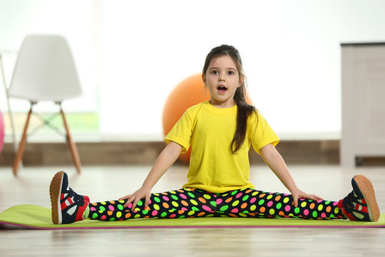 Little cute girl sitting in the splits on a mat indoor
