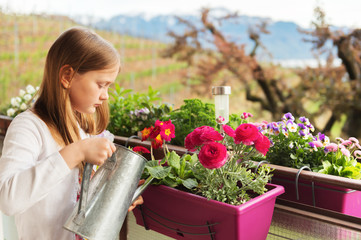Adorable little girl watering flowers on the balcony