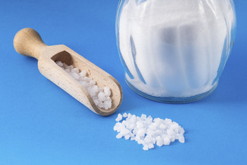 salt crystals with wooden spoon and glass saltshaker on blue background