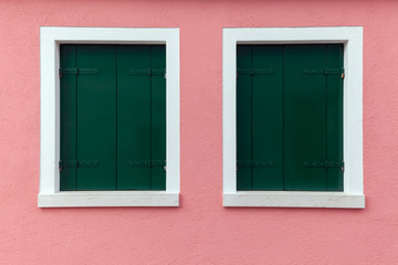 Two old windows with dark green shutters on light pink wall