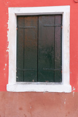 Old window with dark green shutters on red wall