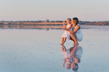 Мама играет с маленькой дочерью в море на закате