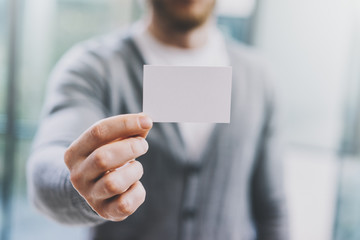 Man wearing casual shirt and showing blank white business card. Blurred abstract background. Horizontal mockup