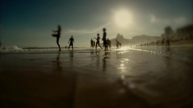 Silhouettes of carioca Brazilians playing altinho beach football at sunset on the shore of Ipanema Beach in Rio de Janeiro, Brazil