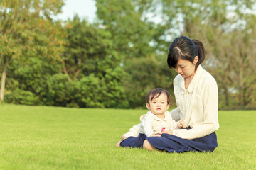 公園の芝に座り赤ちゃんと遊ぶお母さん