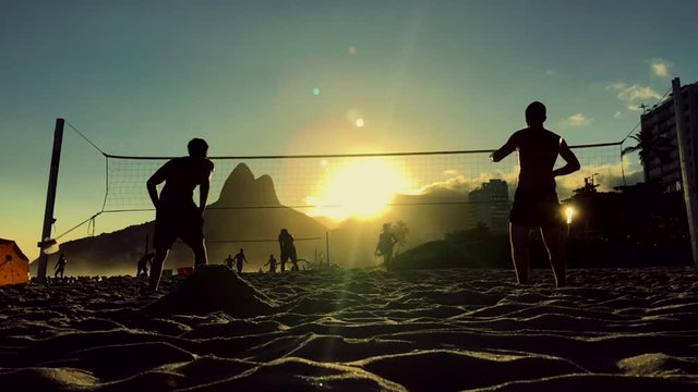 Silhouettes playing Brazilian beach futevolei (footvolley), a sport combining football (soccer) and volleyball, at sunset on Ipanema Beach Rio