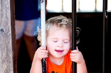 Adorable little toddler girl in pumpkin shirt behind bars.