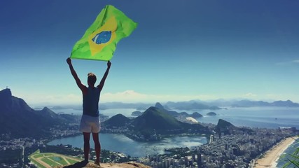 Athlete stands holding a Brazilian flag at a bright overlook of the city skyline of Rio de Janeiro, Brazil