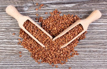 Heap of buckwheat groats with spoon on wooden surface