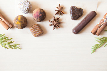 Raw candies made of date fruit,nuts, hibiscus,curry,cocoa,coconut decorated with cinnamon sticks,cardamom,thuja branches on light wooden background indoors.Healthy and raw sweet-shop design content. 