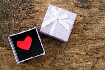 Opened purple gift box on wooden background with red love symbol inside the gift box. Selective focus. Conceptual.
