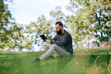 Obraz premium Bearded man hipster student reading a book and relax in park, exams