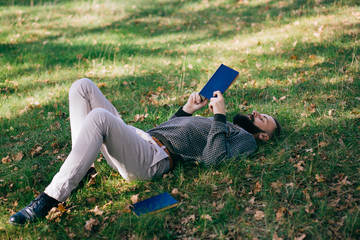 Bearded man hipster student reading a book and relax in park, exams