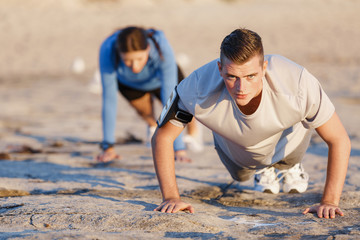 Young couple doing push ups on ocean beach