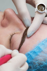Cosmetologist applying permanent make up (tattoo) on eyebrows.