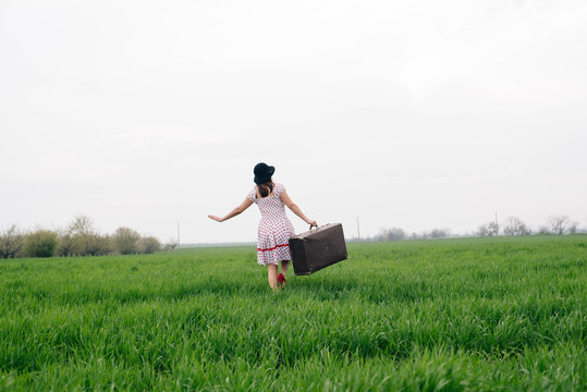 woman in vintage clothes with suitcase in field. Vintage toning