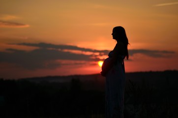 the pregnant girl with a hat in the field of wheat on a sunset