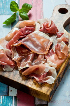 sliced prosciutto on a wooden cut board and rusty wooden background