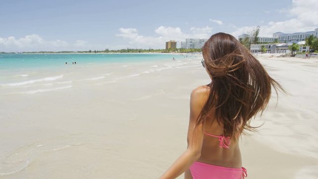 Bikini vacation woman carefree playing with hair walking in the sun sunbathing on Caribbean beach enjoying tropical holidays. American Isla Verde resort in San Juan, Puerto Rico, USA.