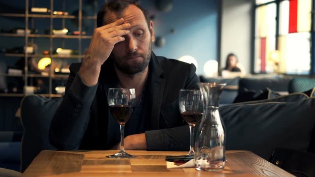 Sad, unhappy man waiting for someone in cafe and drinking red wine
