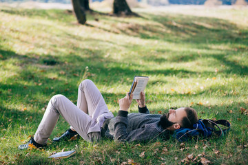 Bearded man hipster student reading a book and relax in park, exams 