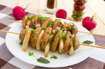 Homemade potatoes baked on a thin stick with bacon and herbs on a wite plate