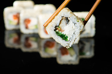 close up of chopsticks taking portion of sushi roll on the table