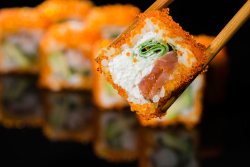 close up of chopsticks taking portion of sushi roll on the table