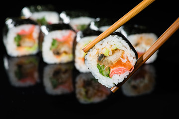 close up of chopsticks taking portion of sushi roll on the table