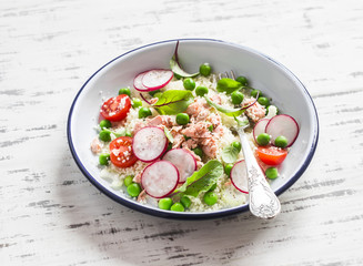 Delicious healthy food - salad with cous cous, fresh vegetables and baked salmon. On a light background
