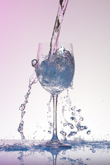 Water pouring into a big size wineglass with many splashes.