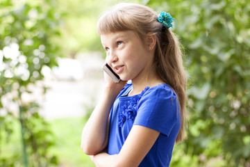 Little girl  summer park talking on the phone, in a blue dress. Blonde