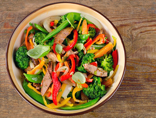Beef stir fry with vegetables on wooden background.