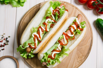 Hot dog with pickles, tomato and lettuce on wooden background