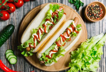 Hot dog with pickles, tomato and lettuce on wooden background