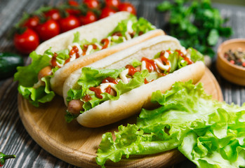 Hot dog with pickles, tomato and lettuce on wooden background